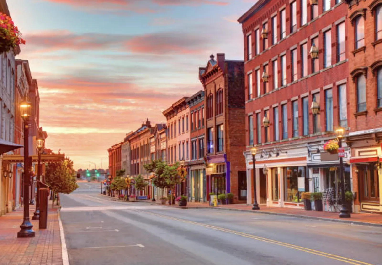 Downtown Norwalk street at dawn lined with restored brick Victorian commercial blocks, ground-floor storefronts, and gas-style street lamps